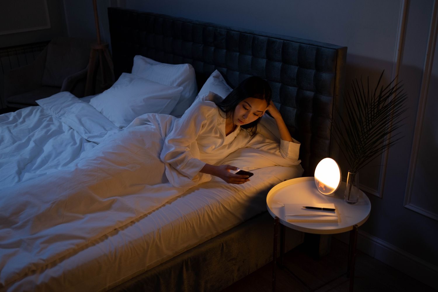 A woman awake at night, lit by her phone